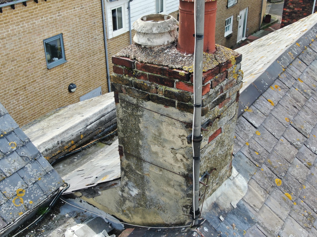 Close-up drone photograph showing damaged roof tiles and potential leak points on chimney stacks